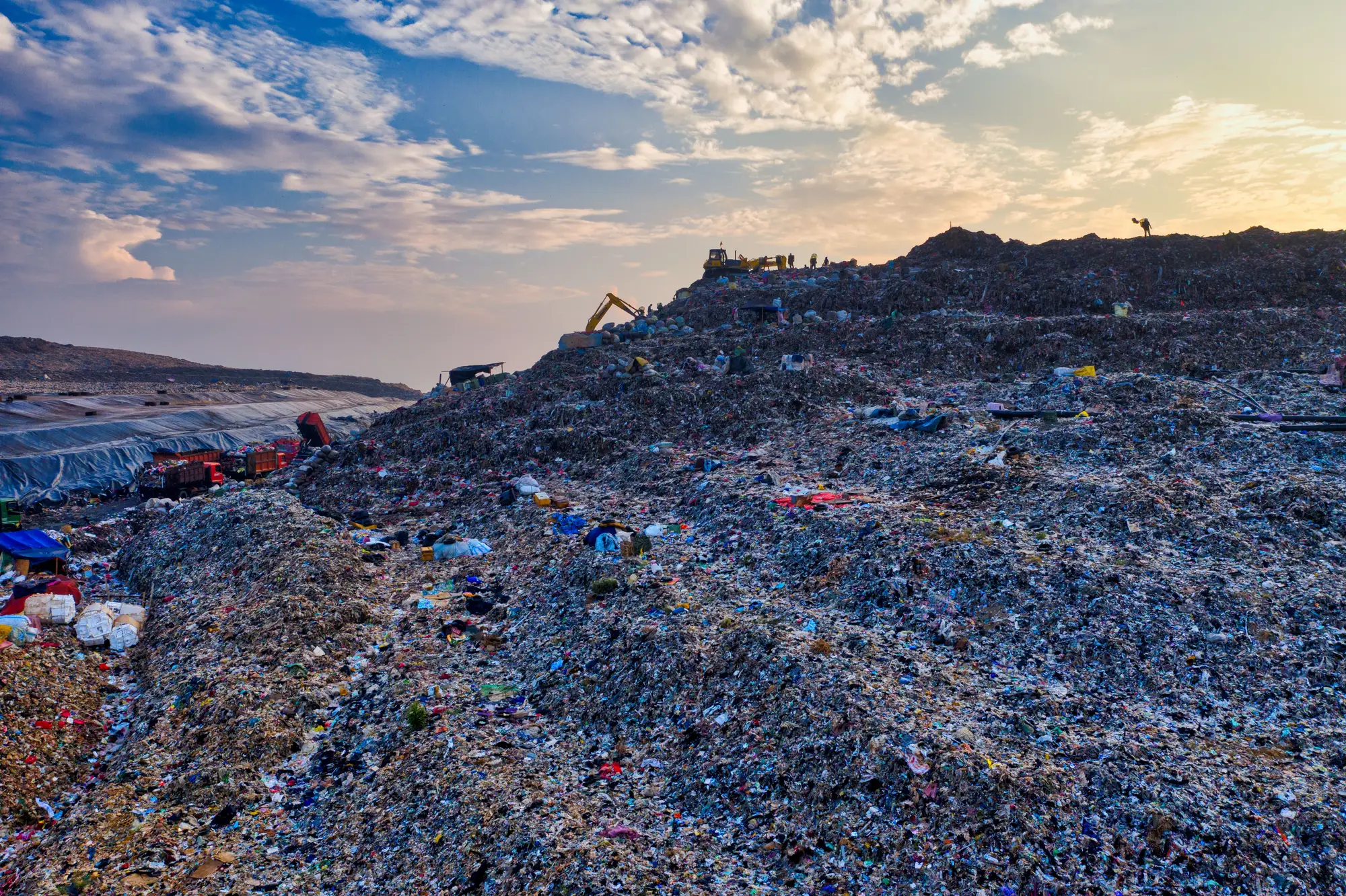 The working slope of a landfill mound at dusk, machines small on the ridge line